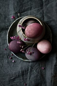 some pink and purple eggs in a bowl on a black table cloth next to flowers