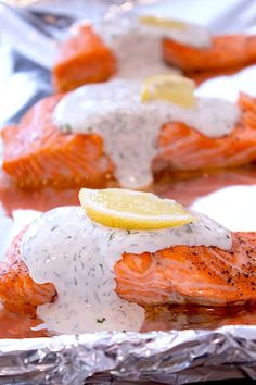 three salmon fillets with lemon and dill on top, sitting on tin foil