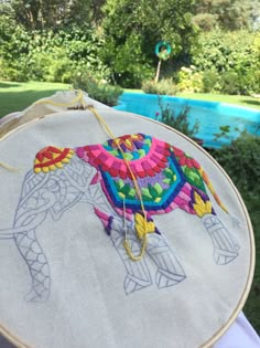 a colorful elephant on a white cloth is being stitched onto an embroidery hoop by someone's hand