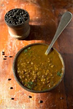 a bowl filled with beans next to a spoon on a wooden table and another container full of black lentils in the background