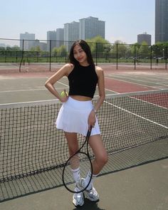 a young woman holding a tennis racquet on top of a tennis court with buildings in the background