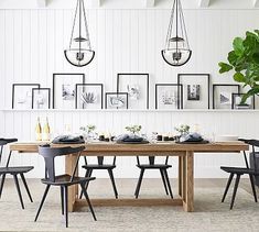 a dining room table with chairs and pictures on the wall above it, along with a potted plant