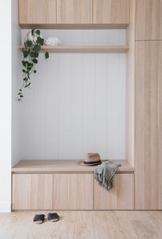 a hat, slippers and coat hang on a wooden shelf in a white room