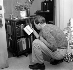 a black and white photo of a man kneeling down in front of a book shelf