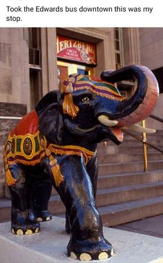 an elephant statue sitting on top of a cement block in front of a building with stairs