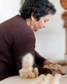 an older woman is sitting on the floor with her hands together and she is knitting