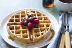 a waffle topped with berries and syrup on top of a white plate next to a fork