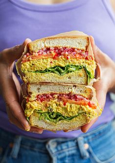 a person holding two sandwiches in their hands with eggs, tomatoes and spinach on them