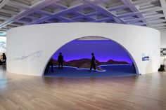 two people are standing in front of an art exhibit with purple lights on the walls