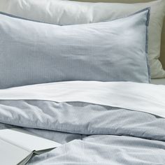 a bed with blue and white sheets, pillows and a laptop on top of it