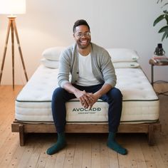 a man sitting on top of a bed in a room with wooden floors and white walls