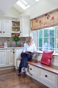 a woman sitting on a window sill in a kitchen reading a book and looking out the window