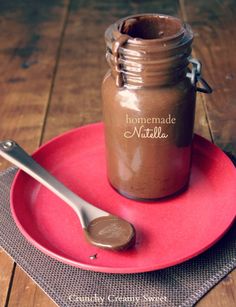 a spoon sitting on top of a red plate next to a jar filled with chocolate