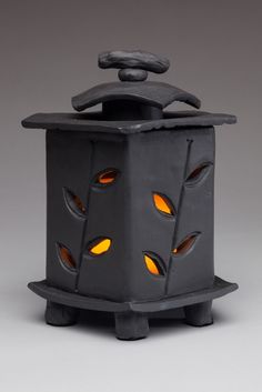 a black candle holder with yellow lights on it's sides and an open lid