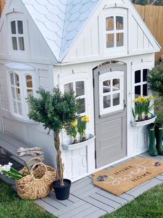 a doll house with potted plants and flowers in the front yard, next to a welcome mat