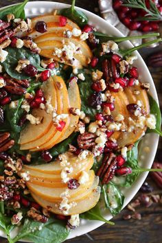 a white bowl filled with spinach, pears and feta cheese topped with nuts