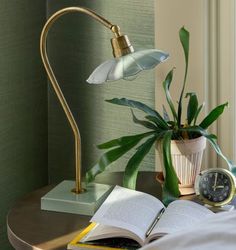 an open book is sitting on a table next to a lamp and a potted plant