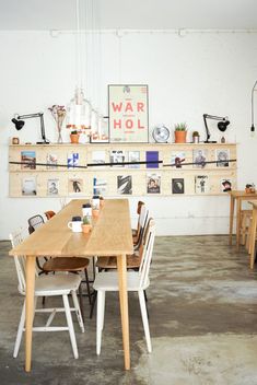 a wooden table surrounded by white chairs in a room with shelves and pictures on the wall