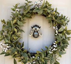 a wreath with a bee on it hanging from the side of a white door,