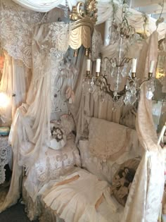 a bed covered in lots of white lace next to a wall mounted chandelier