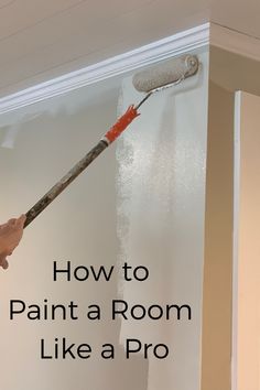 a person painting a room with white paint on the wall and red brush in hand