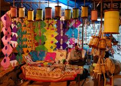 a man sitting in front of a table with many different colored lamps hanging from it