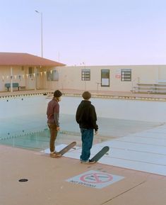 two young men standing in front of a swimming pool with a skateboard on the ground