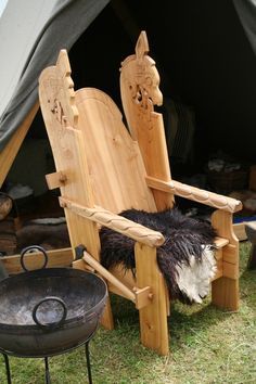 a wooden chair sitting in the grass next to an open fire pit and potted plant