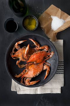 two cooked crabs on a plate with salt, pepper and seasoning next to them