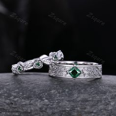 two wedding rings with green stones on them sitting on top of a stone slab in front of a black background