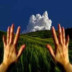 two hands reaching up to the sky above a green field with clouds in the background