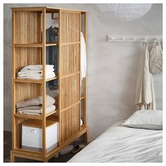 an open bamboo shelf next to a bed with white sheets and blankets on top of it