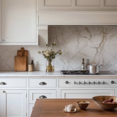 a kitchen with white cabinets and marble counter tops, including a wooden table in front of the stove