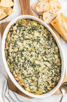 spinach and cheese dip in a white bowl on a cutting board with crackers