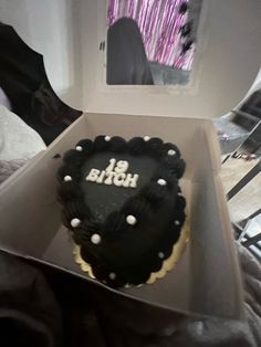 a black and white birthday cake in a box on a bed next to a mirror