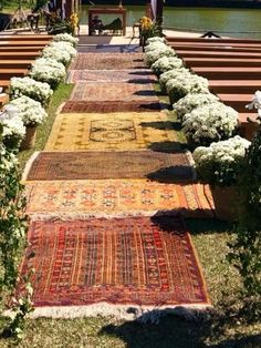 an outdoor area with benches and rugs on the grass near flowers in front of water