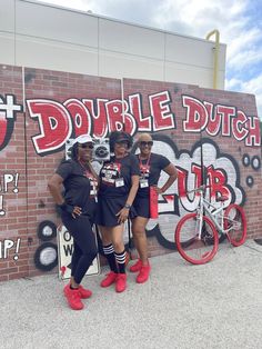 two women standing in front of a brick wall with graffiti on it and one woman wearing red shoes