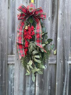 a wreath hanging on the side of a wooden fence with berries and greenery attached to it