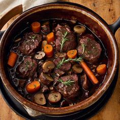 beef stew with carrots and mushrooms in a pot on a wooden table, ready to be eaten