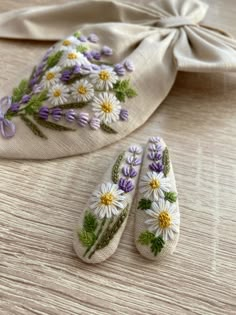 two white slippers with purple and yellow flowers on them next to a beige cloth bag