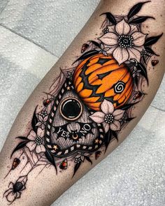 a black and white tattoo with an orange pumpkin in the center, surrounded by flowers