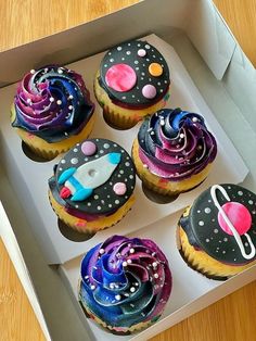 six cupcakes in a box decorated with space themed icing and sprinkles