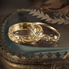 two gold wedding rings sitting on top of a blue satin covered tablecloth next to an ornate frame