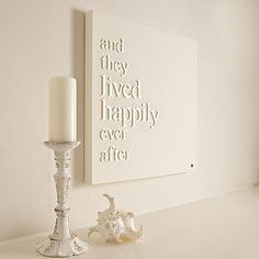 a white candle is sitting on a shelf next to a framed print that says and they lived happily ever after