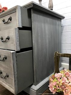 an old dresser has been painted gray and is next to a vase with pink flowers