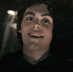 a man with curly hair is smiling and looking up at the sky while wearing a black hoodie