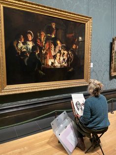 a woman sitting on a chair in front of a painting and looking at it with an easel