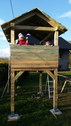 two children sitting on top of a wooden structure in the middle of a yard with green grass