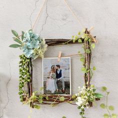 a photo frame hanging on a wall with flowers and greenery around it, holding a couple