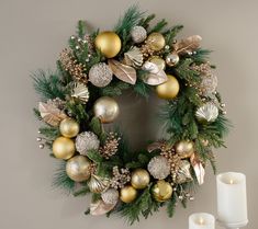 a christmas wreath with gold and silver ornaments next to a lit candle on a table